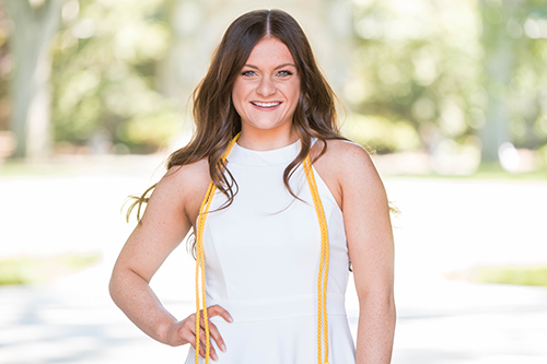 Alexis Roberts in white dress and grad cords outside on sunny day